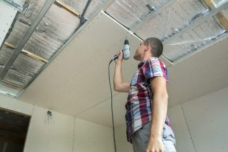 Homme en tenue de travail posant un plafond tendu à Caen